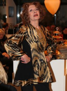 31-03-2013 SHOWBIZZ; SHEILA DE VRIES GEEFT EXCLUSIEVE AVONDSHOW. AMSTERDAM - Het is akelig koud de hele week. Een snijdende wind, constateerde fashiondesigner Sheila De Vries die een exclusieve avondshow geeft voor haar klanten in haar winkel Sheila & Gideon Collections in de Cornelis Schuytstraat. Maar ondanks het ijskoude weer presenteren wij vanavond toch veel lange luchtige zomerjurken met een lage rug. Sheila De Vries werd onder meer bekend door de prachtige couture die zij ontwerpt voor Koningin Beatrix. Iedereen wacht met spanning op De Jurk van 30 april. Maar vanavond wordt haar show gepresenteerd door ... de actrices van Purper.
Zij laten in haar winkel in de hoofdstad haar nieuwe collectie zien. Met veel lange jurken en kaftans voor iedere maat en figuur. Van slankmakende voile en kantachtige materialen. Sheila reist de hele wereld af voor deze unieke stoffen waarvan zij zeer verschillende creaties maakt. Deze keer adviseert zij haar klanten voor de zomer altijd iets van zwart en wit in de kast te hebben. En dat mag ook best in een dessin zijn uitgevoerd.
Sheila maakt prachtige feelgood-jurken die iedere vrouw zowel op een gala als op een avond thuis fasntastisch staan. Jasjes met een meesterlijk dessin, bijzondere tassen, schoenen en sieraden naar eigen ontwerp. En Gideon toont markante jacks voor de moderne man. 
Alle actrices van Purper hebben hun eigen onnavolgbare manier om de creaties van Sheila aan de klanten te tonen. De markante verschijning van Gerrie Van der Klei is onvergetelijk als zij tijdens haar ronde in een lange krijtwitte en rechte jurk van opengewerkt materiaal vol waardigheid met een grote donkere bril op snel een slokje uit een glas wijn gapt. Zoiets zul je een echte mannequin nooit zien doen. Celine Purcell met haar grappige uitstraling is eenvoudig zichzelf.
Ook de blonde Mylou Frencken maakt tijdens deze show wat vrolijke danspassen die herinneren aan de Zumba van de sportschool. Enkele van de klanten van Sheila vertellen mij tijdens de afterparty deze show zo waarderen omdat hier nu eens dames met echte rondingen te zien zijn die ieder hun eigen stijl hebben... Dat klopt want de mysterieuze gratie van professionele mannequins is echt een vak apart. Toch weet Sheila s muze Anouk Van Nes als getraind danseres in een lange zwarte galajurk deze stijl met haar bijzondere flair goed te presenteren.
Het publiek houdt af en toe de adem in bij deze bijzondere Purper-presentatie. Maar hoe verrassend is dit theaterseizoen waar in plaats van vier heren in rokkostuum nu eens een groep van vier vrouwen in rok op de buhne als Purper optreedt. Vier dames die van wanten weten! De Purper Ladies zijn Gerrie Van der Klei, Anouk Van Nes, Celine Purcell en Mylou Frencken.
Vier vakvrouwen ook die hun sporen in het theater ruimschoots hebben verdiend en garant staan voor topkwaliteit, passend bij de Purper traditie. Een traditie die zich in het komend seizoen zal vernieuwen en verdiepen. Vrouwen van verschillende leeftijd en achtergrond die het publiek een avondlang zinnig entertainen. Vrouwen met lef, gein en geweldige stemmen. Het moet een Purper op haar best worden. Uniek. Als genre op zich, niet te imiteren.
Thema: Hoe staan vrouwen van verschillende leeftijden vandaag de dag in het leven? Een onderwerp dat met een gezonde dosis zelfspot tot een hilarische theateravond zal leiden. 
Fasten your seatbelts: de Purper Ladies komen eraan! Het wordt een heerlijk avondje uit!
foto: Albert den Iseger.